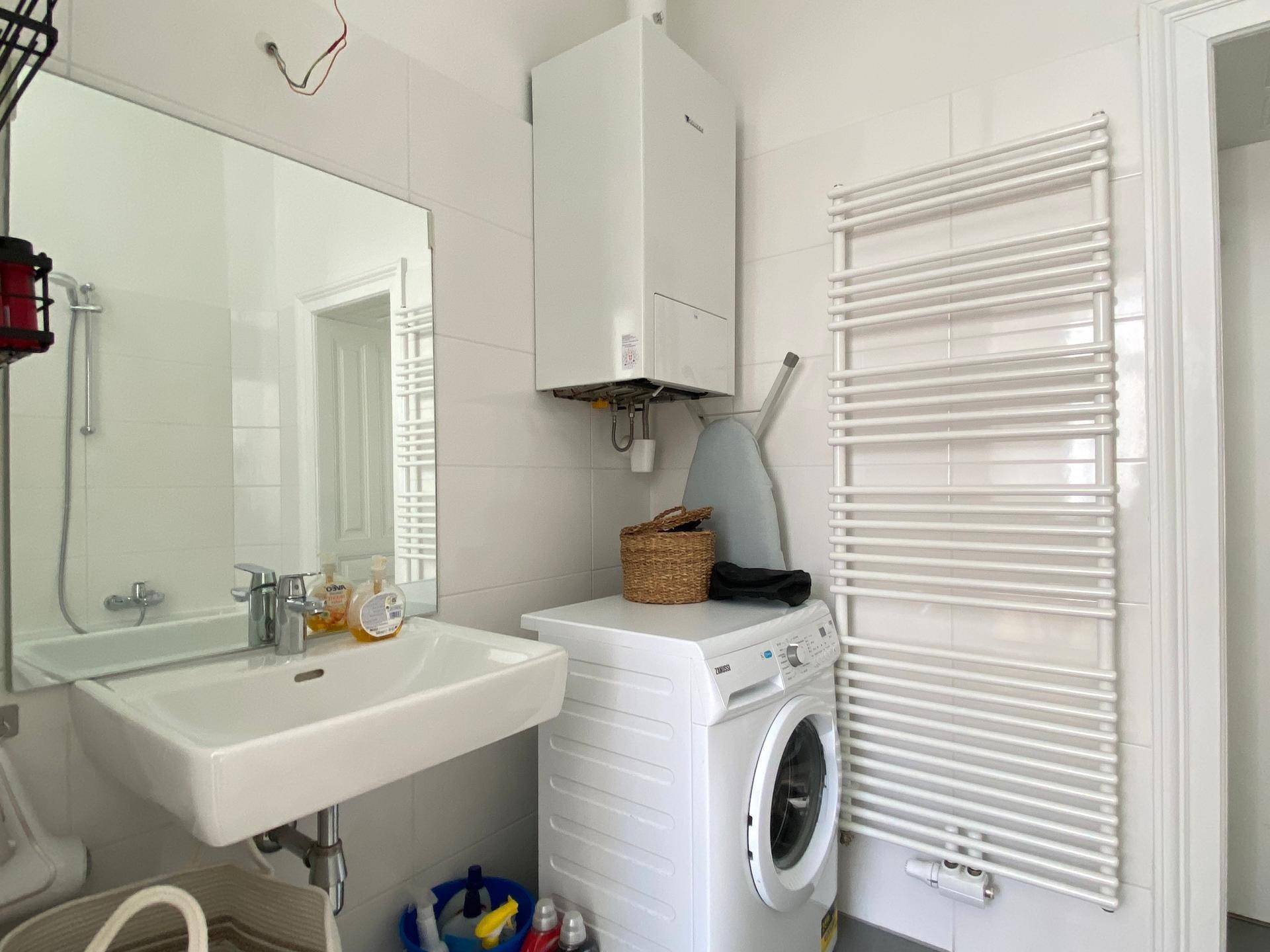 Badezimmer mit Waschbecken, großem Spiegel, Waschmaschine und Warmwasserboiler.