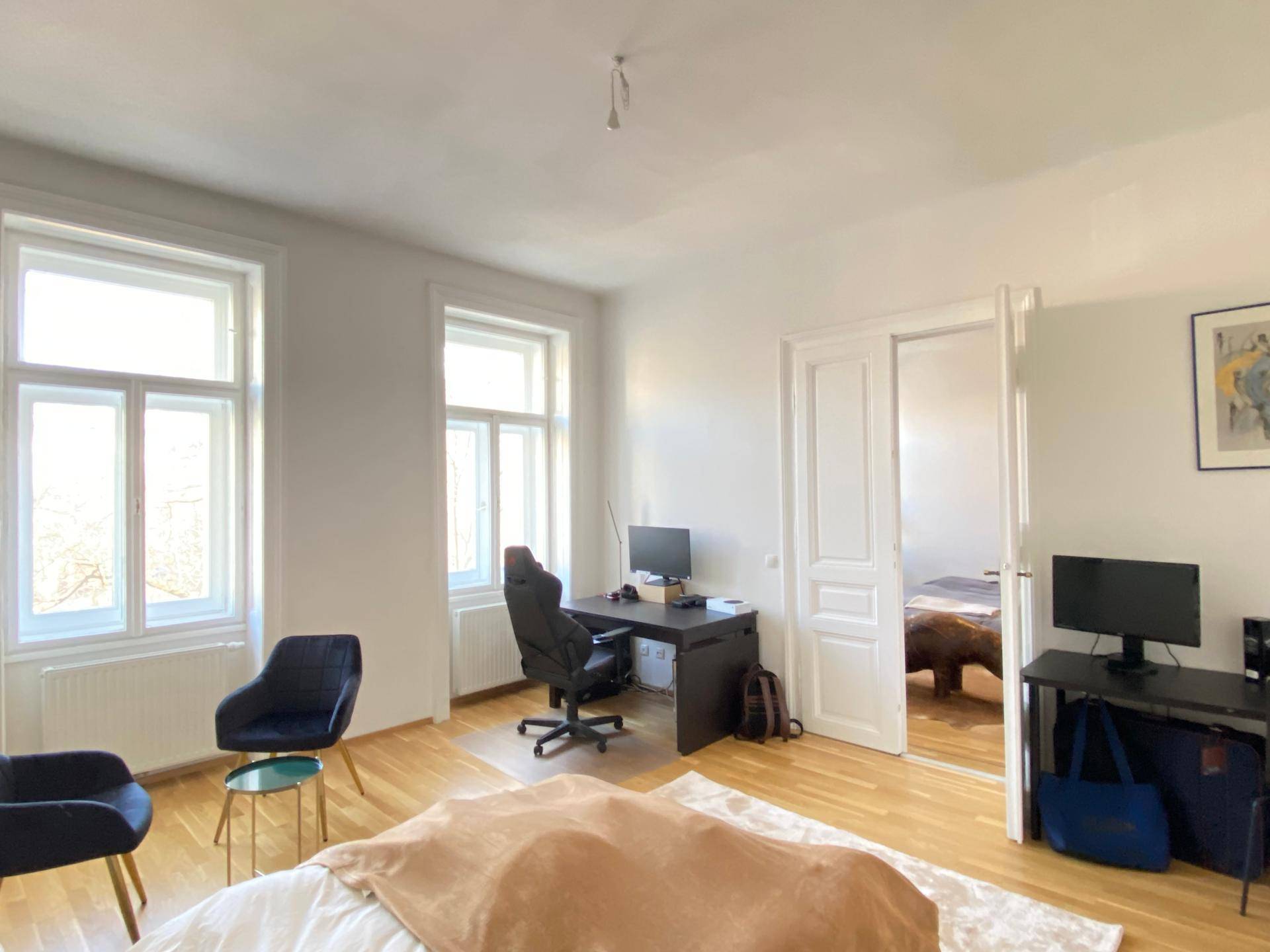 Schlafzimmer mit Arbeitsbereich, Holzboden und Blick durch die Tür in ein weiteres Zimmer.