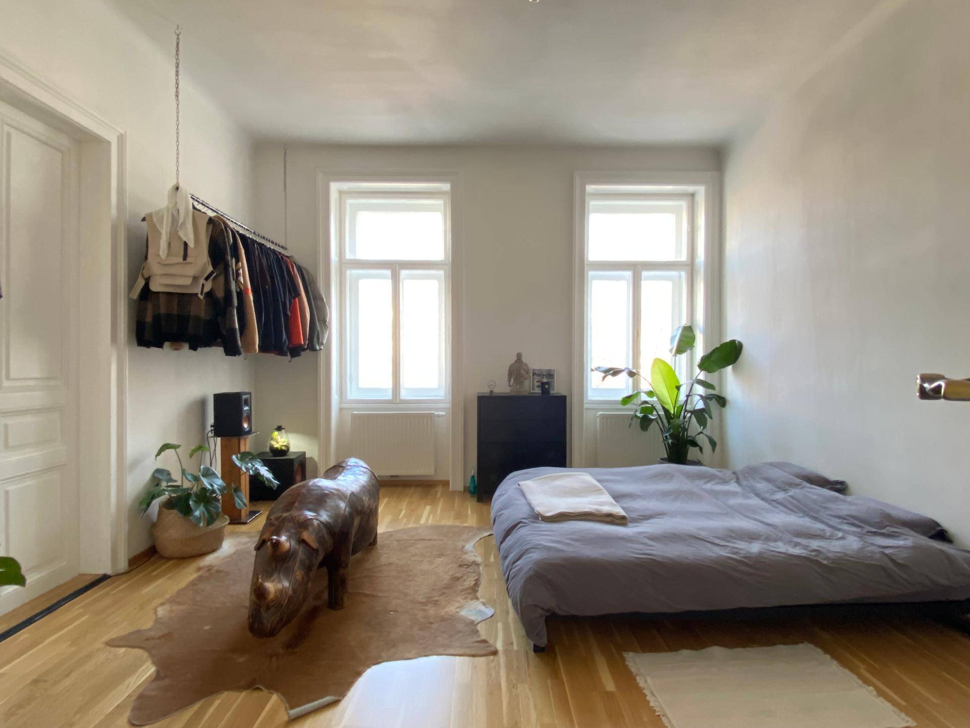 Schlafzimmer mit Holzboden, niedrigem Bett, Kleiderstange und dekorativer Nashornfigur.