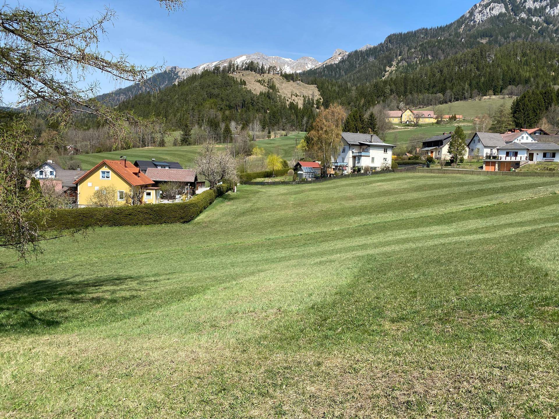 Panoramablick über grüne Felder auf eine malerische Berglandschaft mit vereinzelten Häusern.