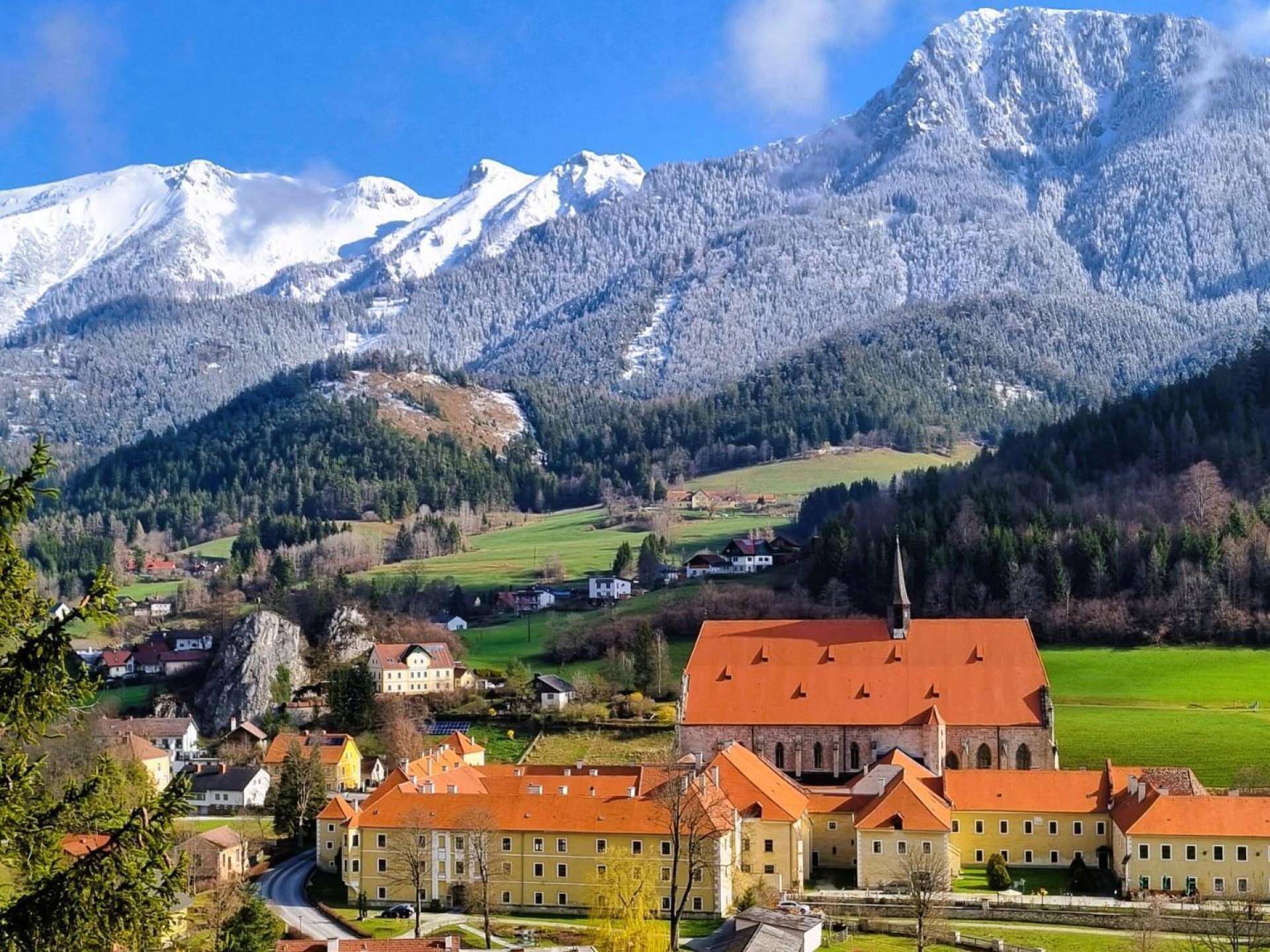 Malerisches Dorf mit historischem Klostergebäude vor der Kulisse schneebedeckter Berge.