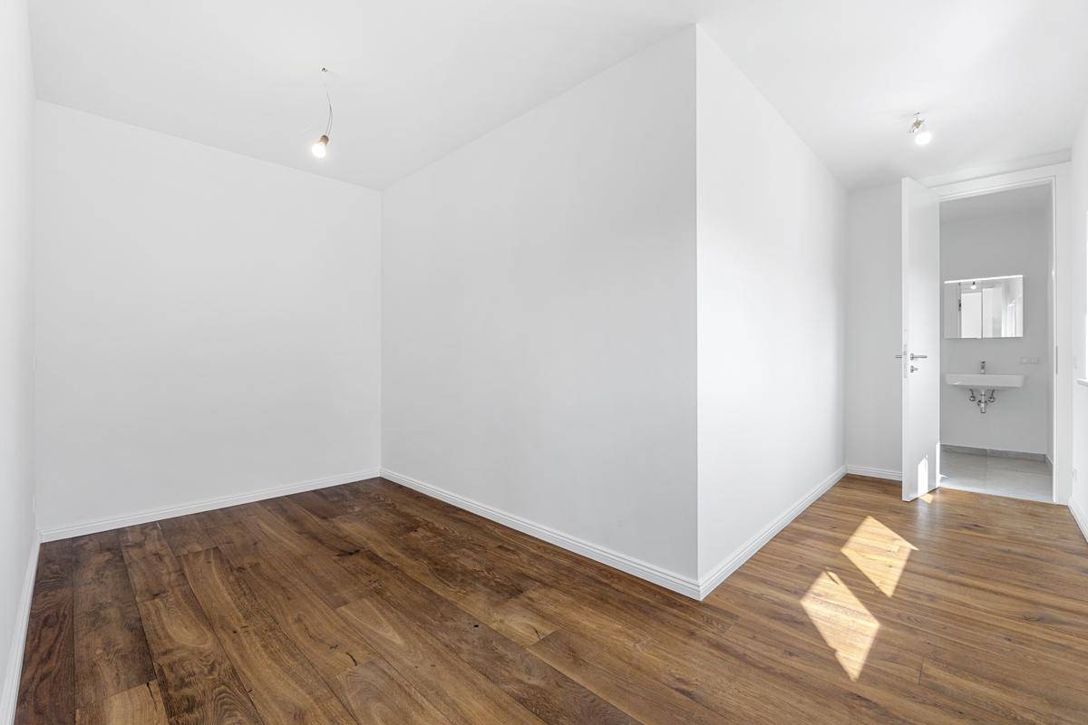 Leeres Zimmer mit Holzboden und weißen Wänden, das viel natürliches Licht durch die Tür erhält.