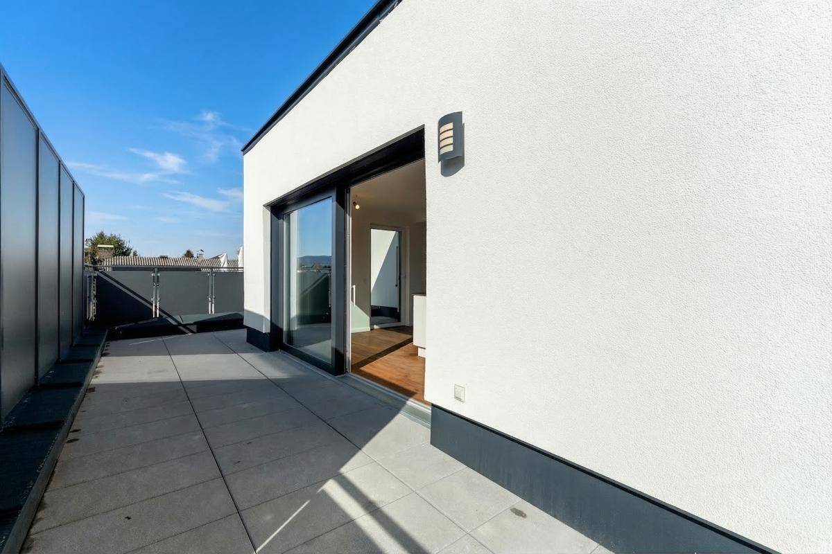 Geräumige Dachterrasse mit Fliesenboden und Schiebetür, die Zugang zum Innenbereich bietet.