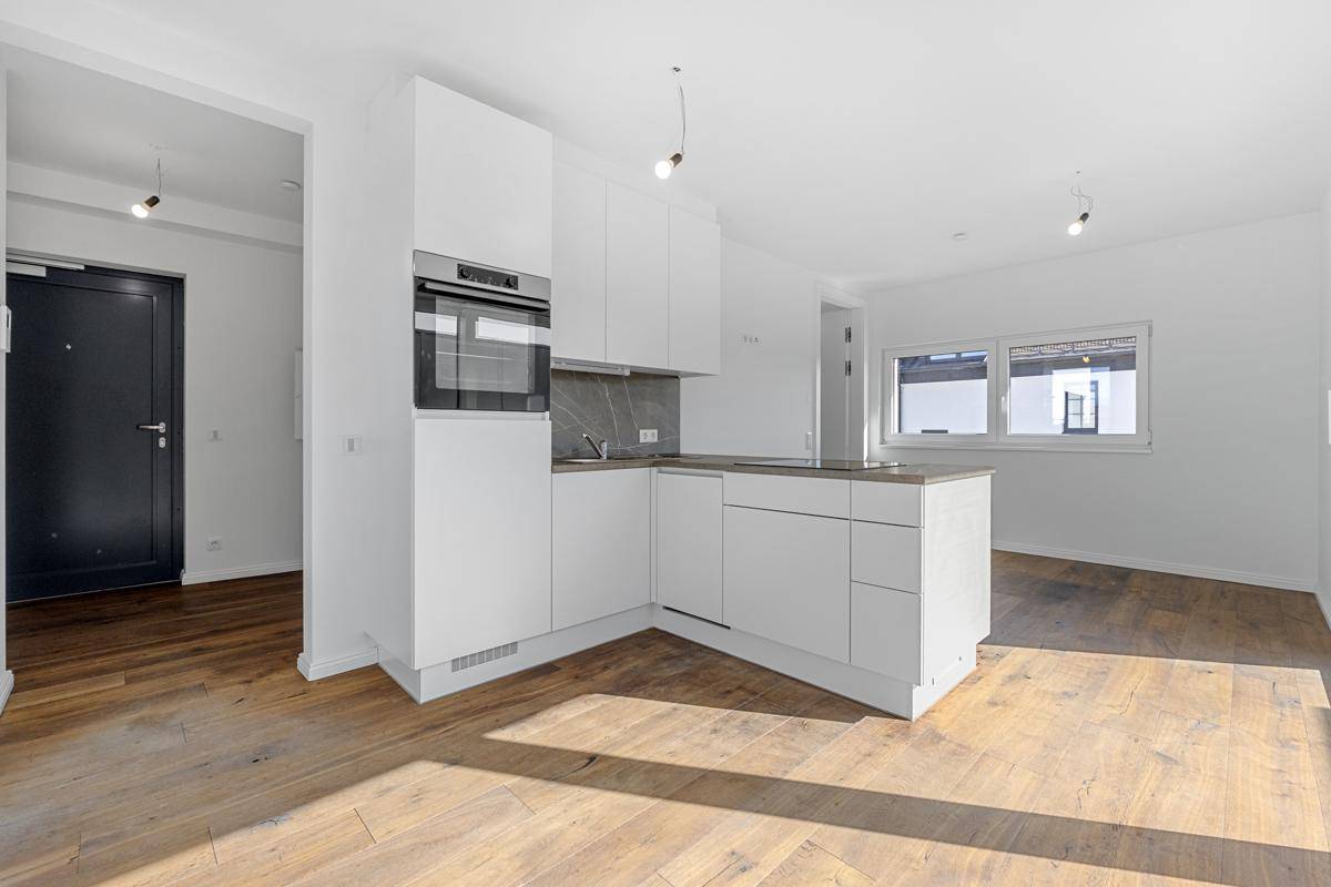 Moderne weiße Küchenzeile mit integriertem Backofen und Holzboden in einem hellen Wohnbereich.
