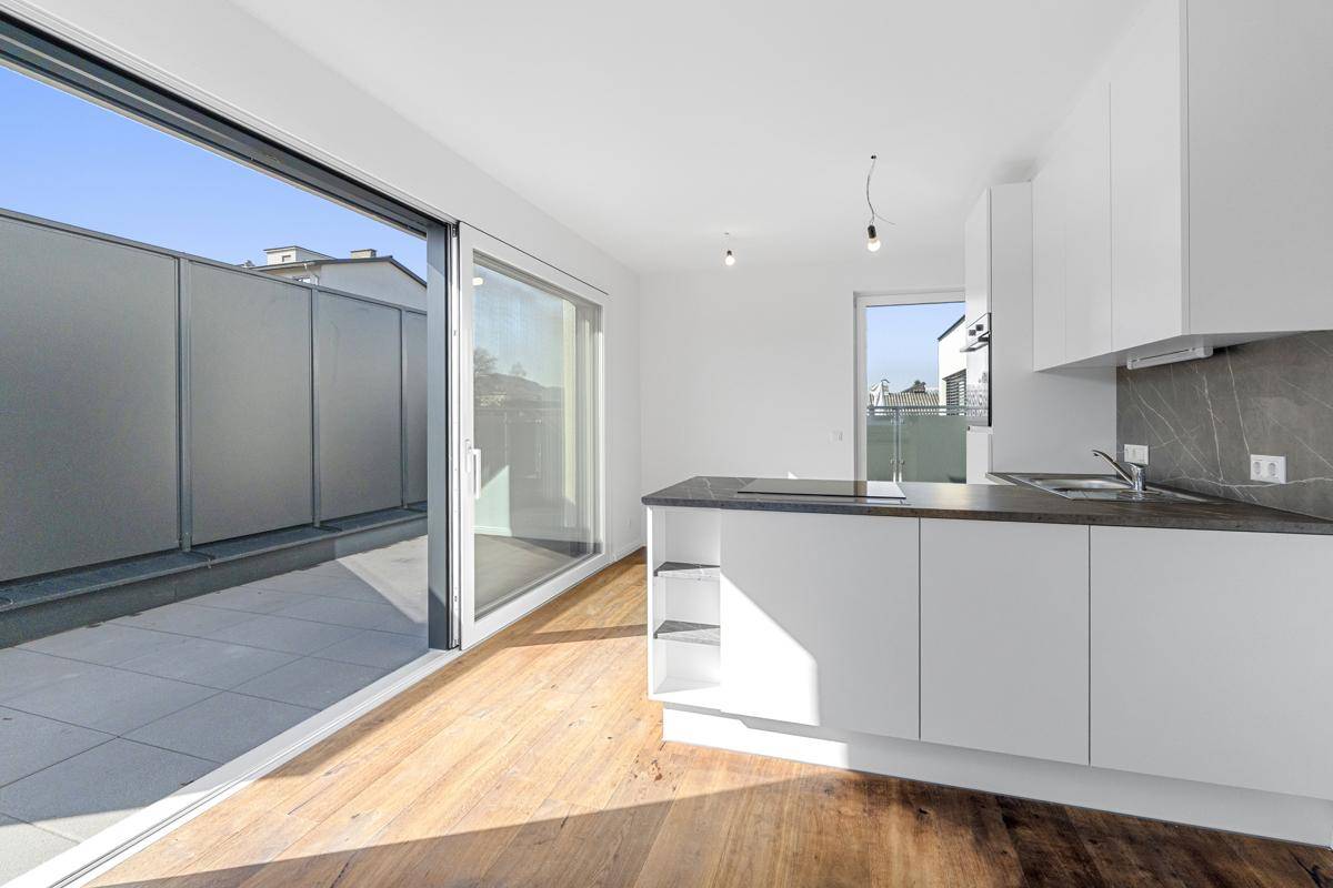 Offene Küche mit weißer Einrichtung und Holzboden, die durch eine große Schiebetür zur Terrasse führt.