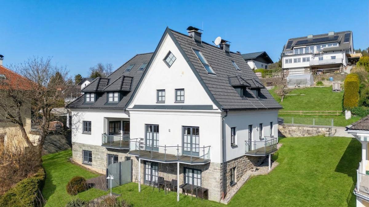 Seitenansicht des modernen Hauses mit mehreren Balkonen und terrassiertem Garten.