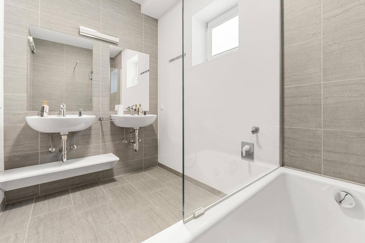 Modernes Badezimmer mit doppelten Waschbecken, Badewanne und grauen Fliesen.
