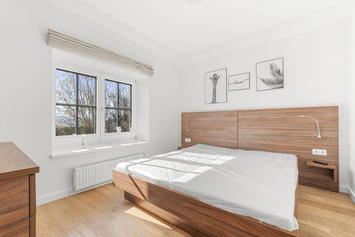 Helles Schlafzimmer mit Holzbett, Parkettboden und Fenster mit Blick ins Grüne.