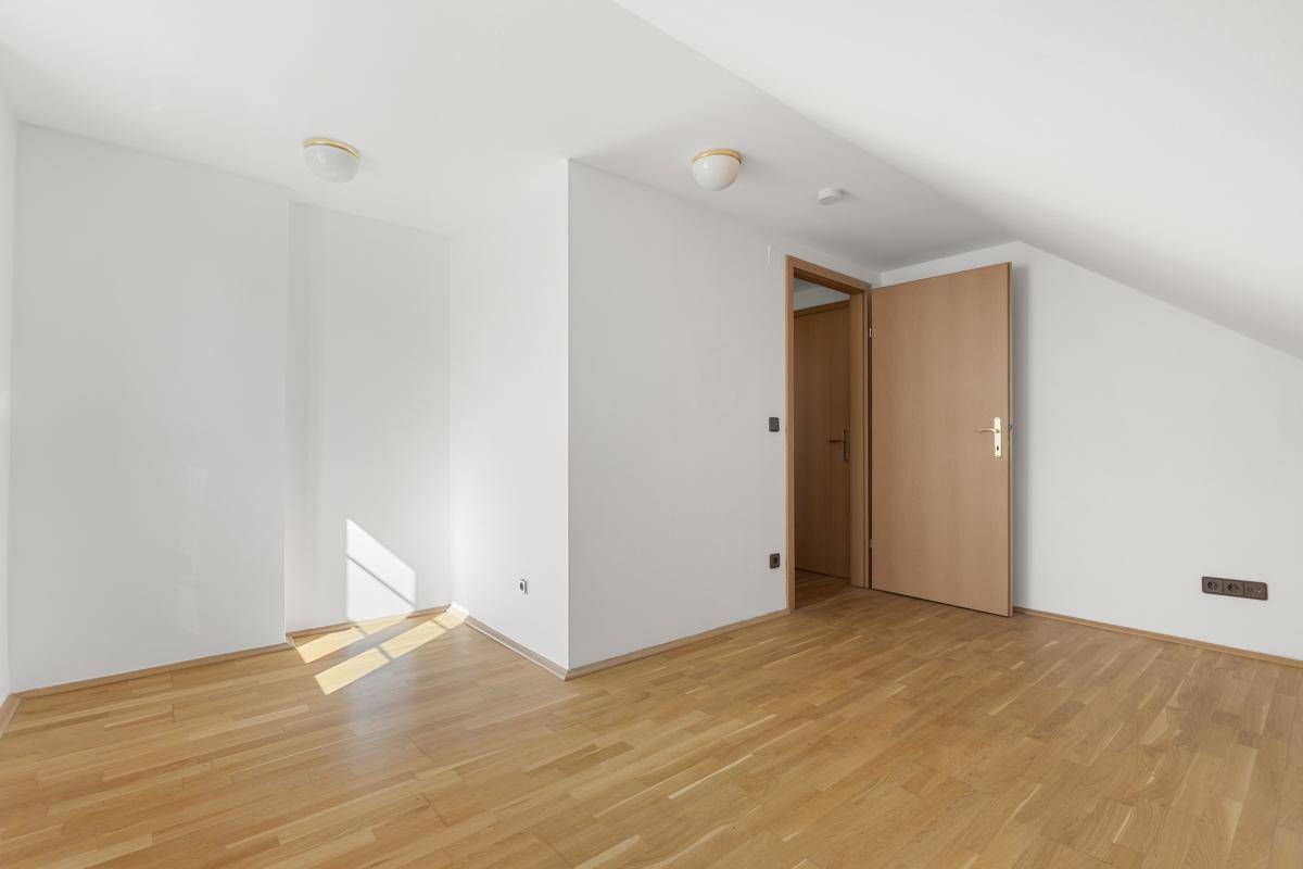 Leeres Zimmer im Dachgeschoss mit Holzboden, weißen Wänden und schräger Decke.