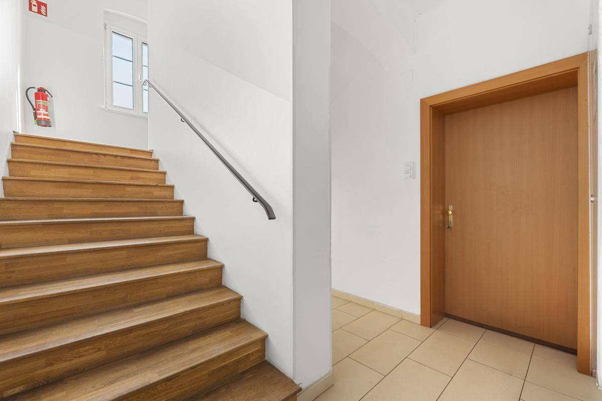 Heller Treppenaufgang mit Holzstufen und Fliesenboden im Eingangsbereich.