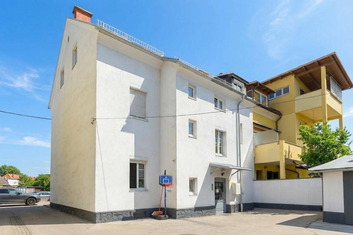 Seitenansicht des weißen Wohnhauses mit Basketballkorb und angrenzendem gelbem Gebäude.