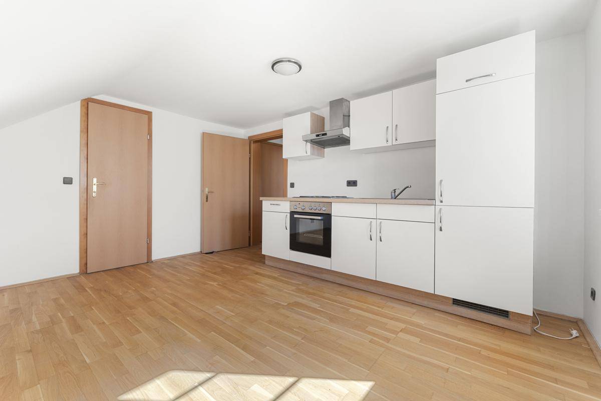 Kleine Einbauküche mit weißen Schränken und Herd in einem hellen Raum mit Holzboden.