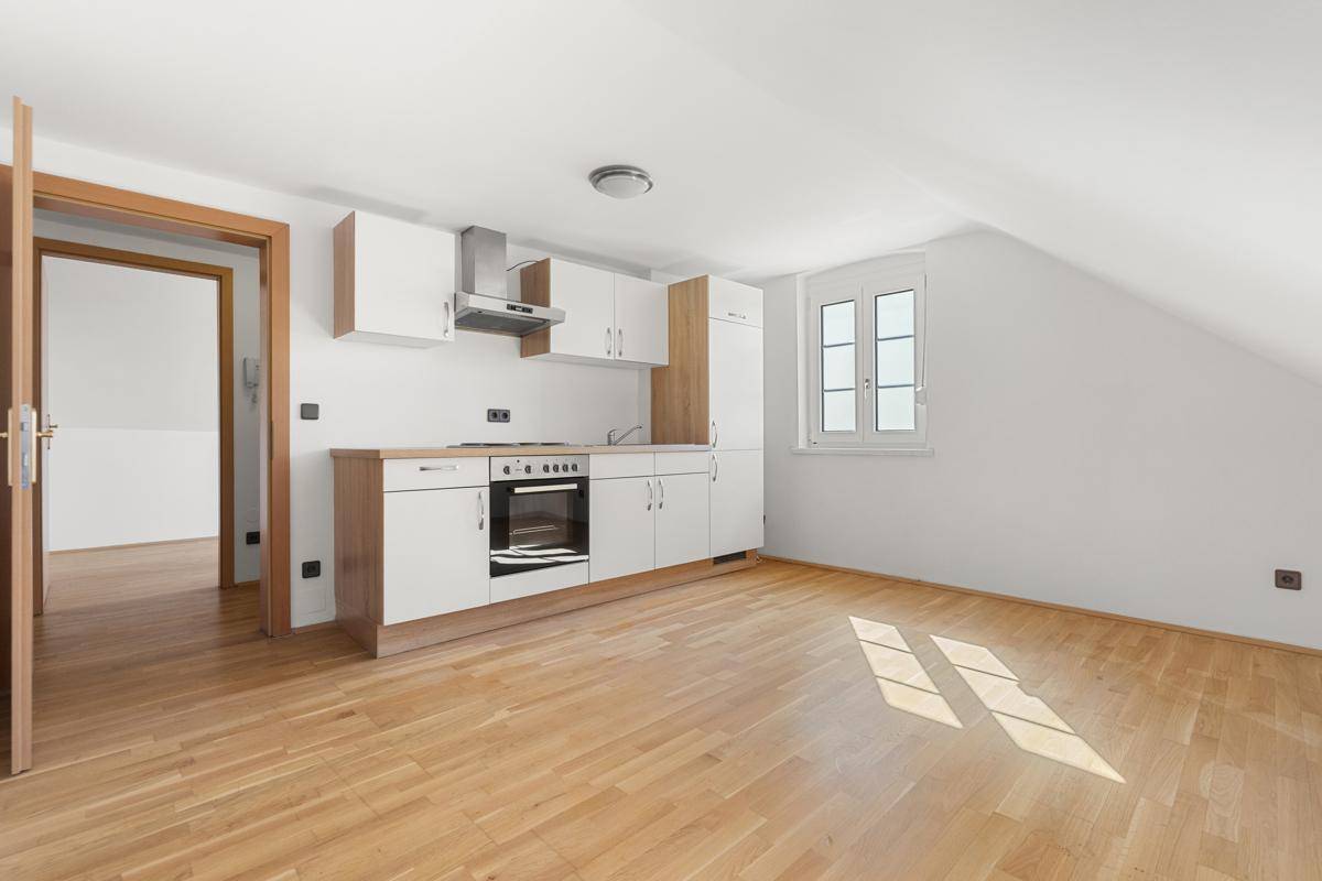 Helle Küchenzeile mit Fenster und Holzboden in einem Dachgeschossraum mit schräger Decke.