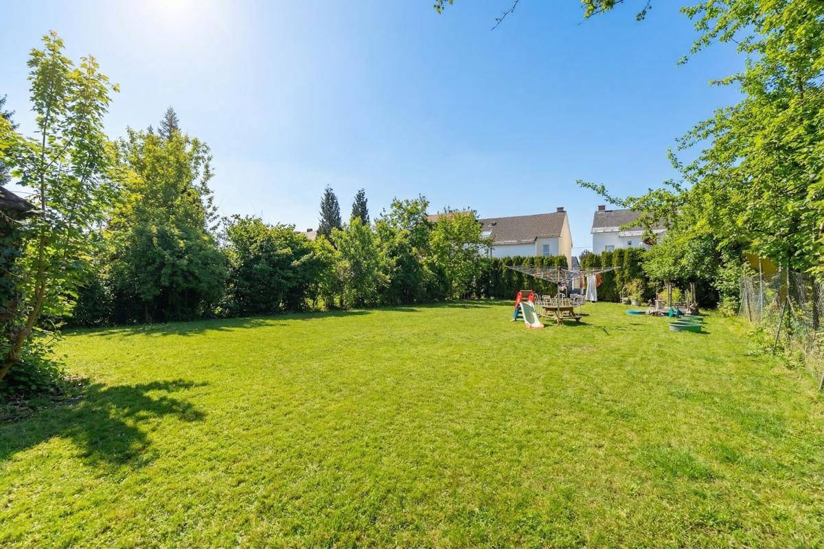 Großer, gepflegter Rasengarten mit Spielgeräten und umgebenden Bäumen unter blauem Himmel.