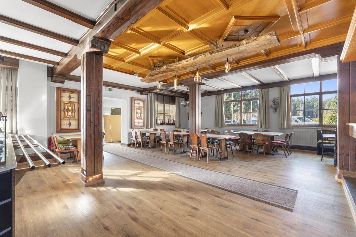 Geräumiger Speisesaal mit Holzbalken, Holzboden und vielen Tischen für Gäste.