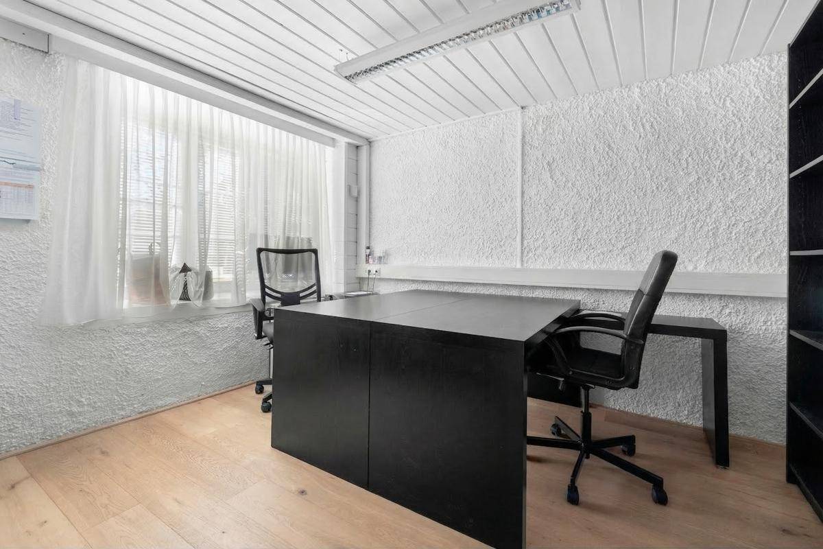 Helles Büro mit Holzboden, strukturierten Wänden und großem Fenster.