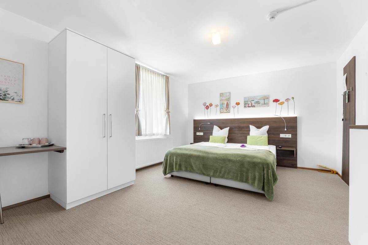 Helles Schlafzimmer mit Doppelbett, Teppichboden und modernen Wanddekorationen.