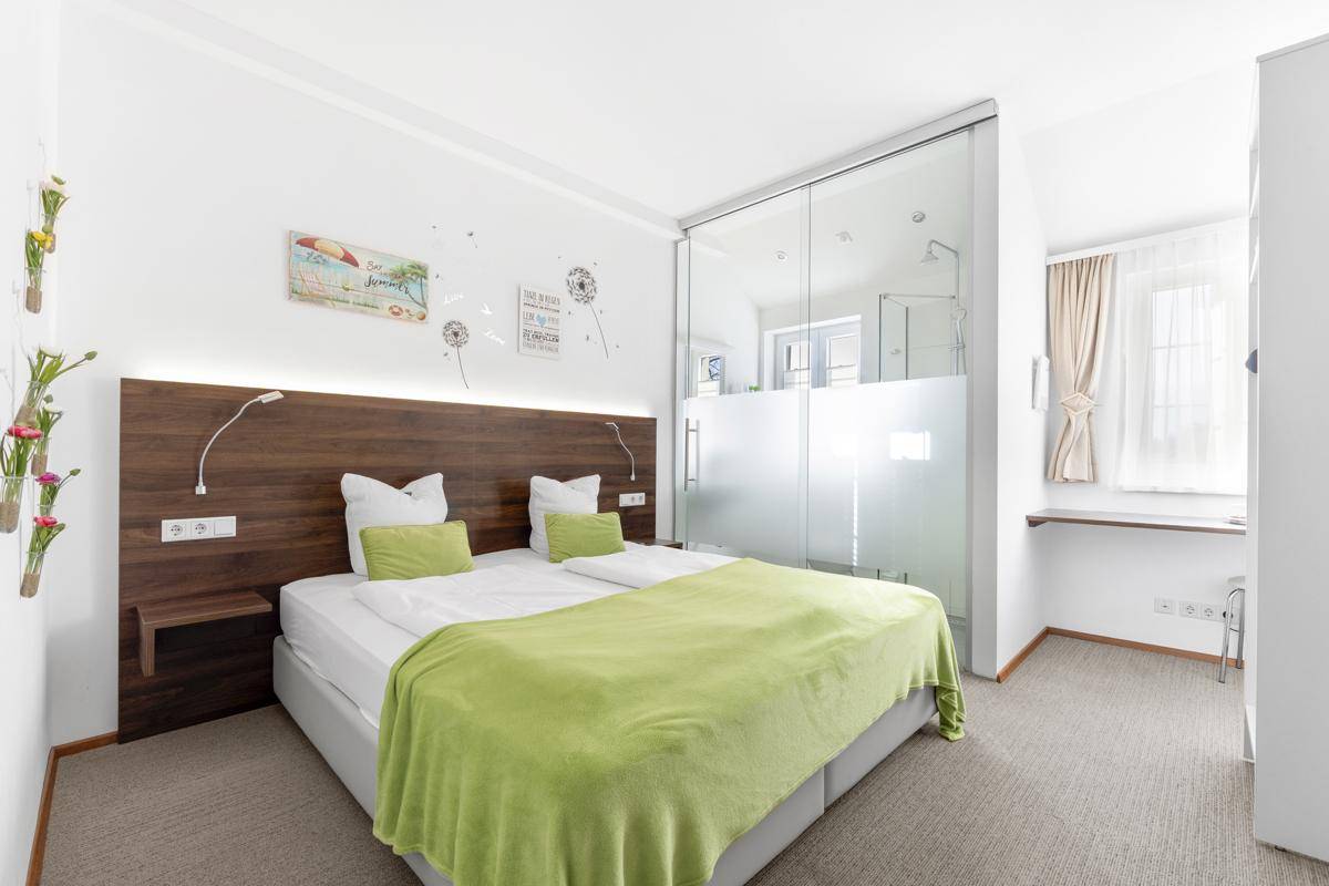 Komfortables Schlafzimmer mit Doppelbett und integriertem Badezimmerbereich mit Glaswand.