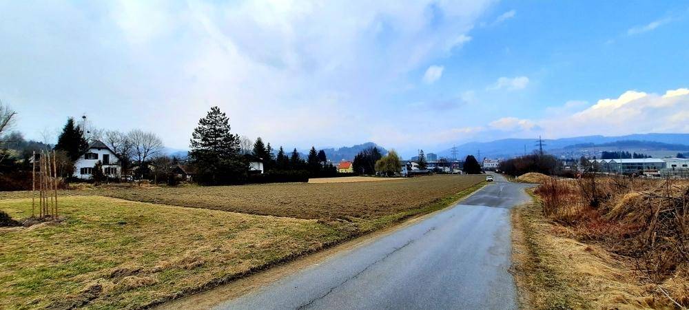 Blick über ein Feld und eine Straße auf die umliegende ländliche Landschaft mit Bergen am Horizont.