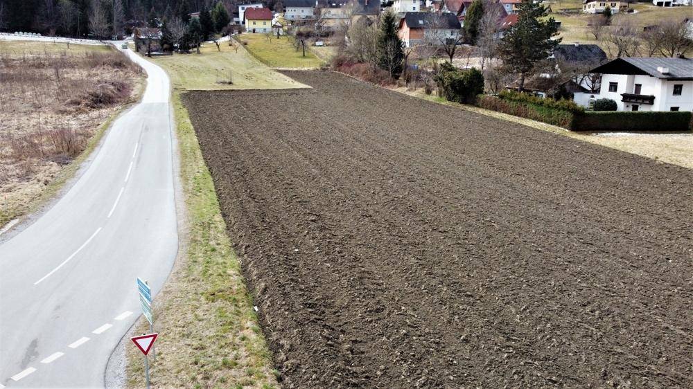Übersicht des unbebauten Grundstücks mit angrenzender Straße und ländlicher Umgebung unter bewölktem Himmel.