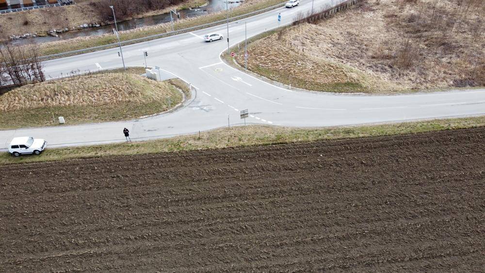 Luftaufnahme einer Straßenkreuzung neben dem Grundstück mit Fahrzeugen und ländlicher Umgebung im Vordergrund.