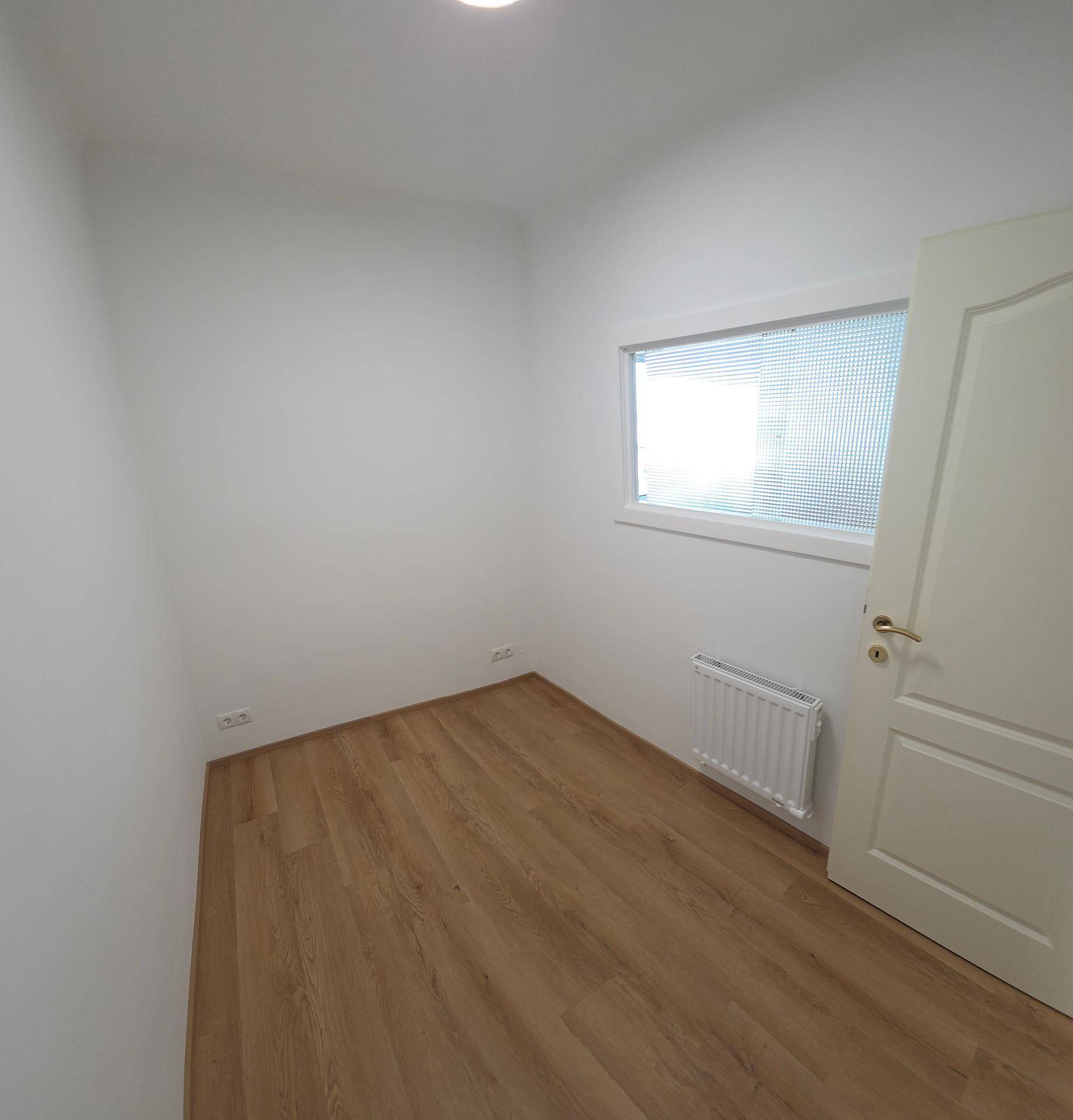 Kleines, helles Zimmer mit Laminatboden und einem Fenster mit Milchglas für Privatsphäre.