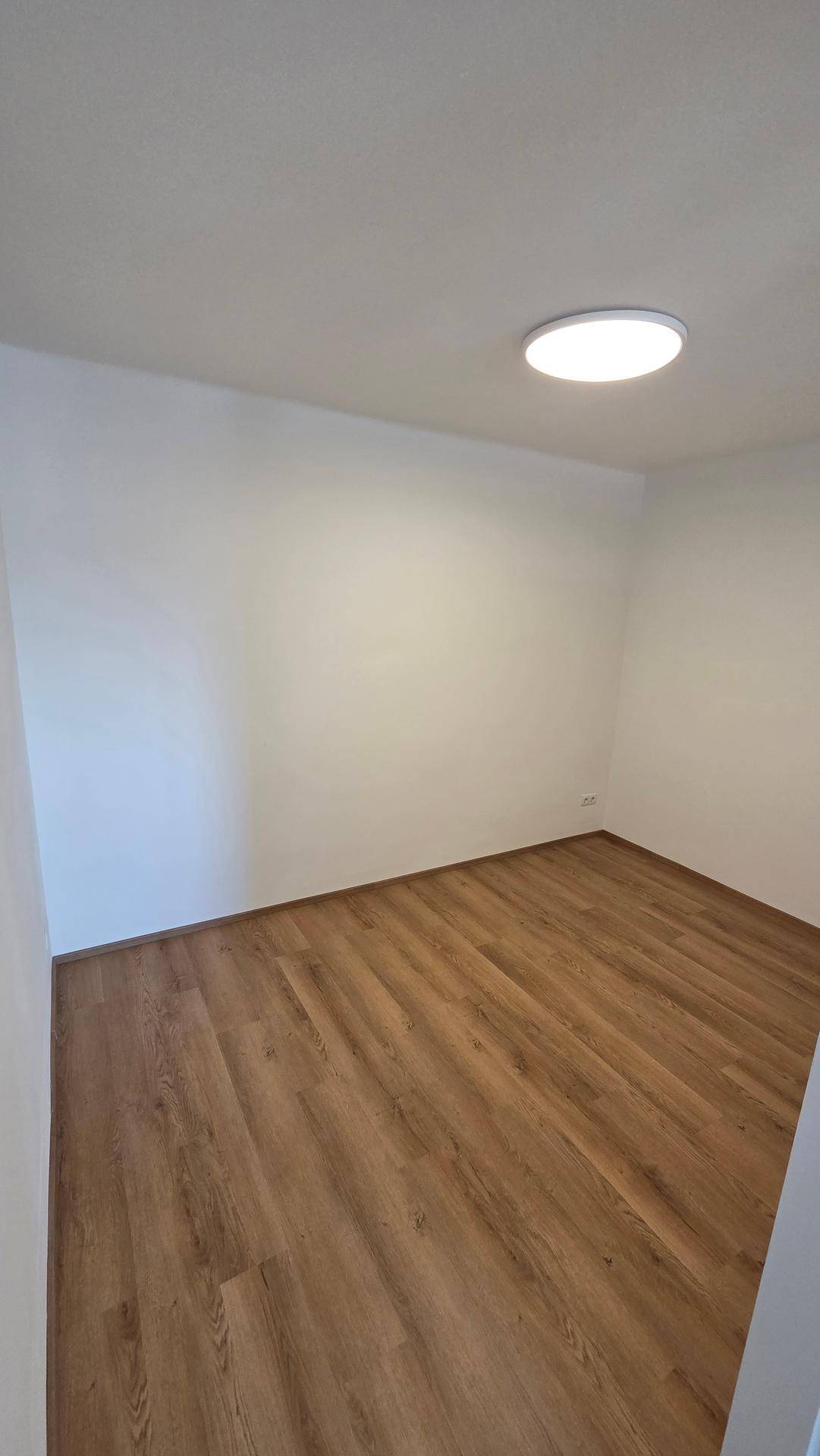 Helles, leeres Zimmer mit Laminatboden und weiß gestrichenen Wänden, bereit zum Einrichten.