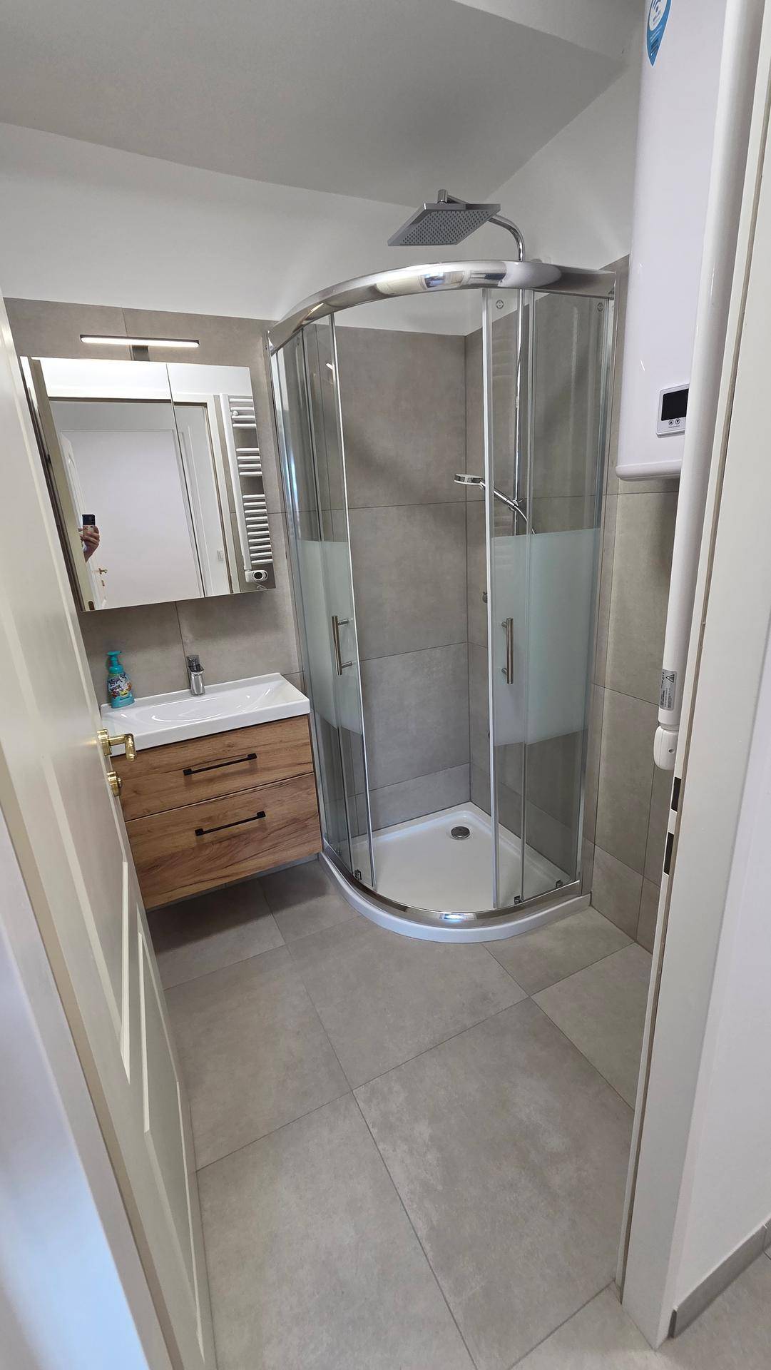 Modernes Badezimmer mit Duschkabine, Holzwaschtisch und grauen Fliesen, inklusive Spiegelschrank.