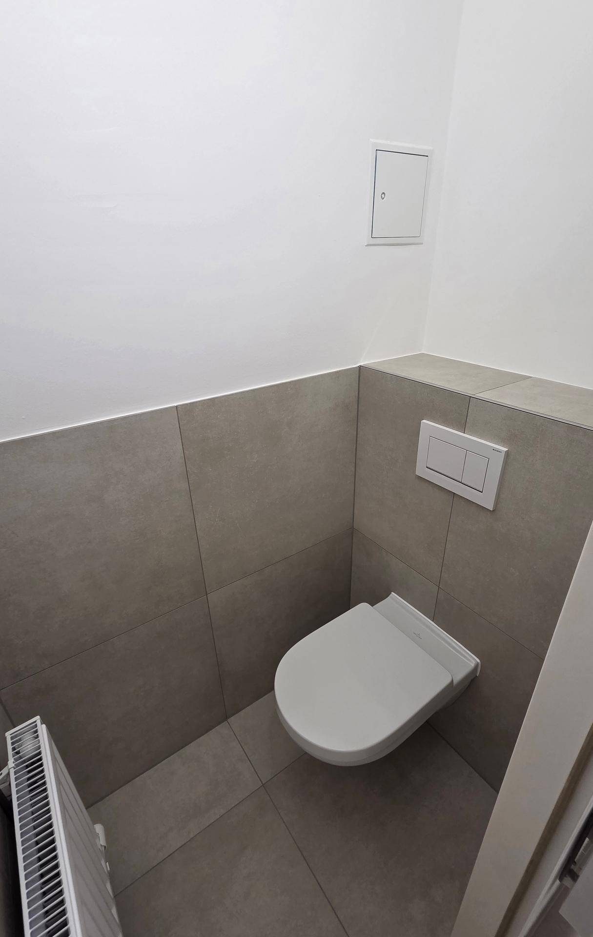 Separates WC mit Wand-WC und grauen Fliesen, ausgestattet mit einem Heizkörper für Komfort.