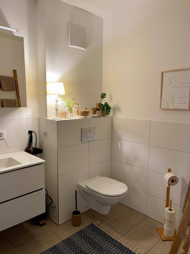 Modernes Gäste-WC mit Wand-WC, kleinem Waschbecken und weißen Fliesen.