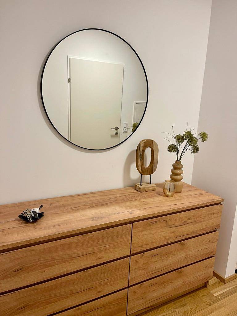 Holzkommode mit rundem Spiegel und schlichter Dekoration in einem hellen Flurbereich.