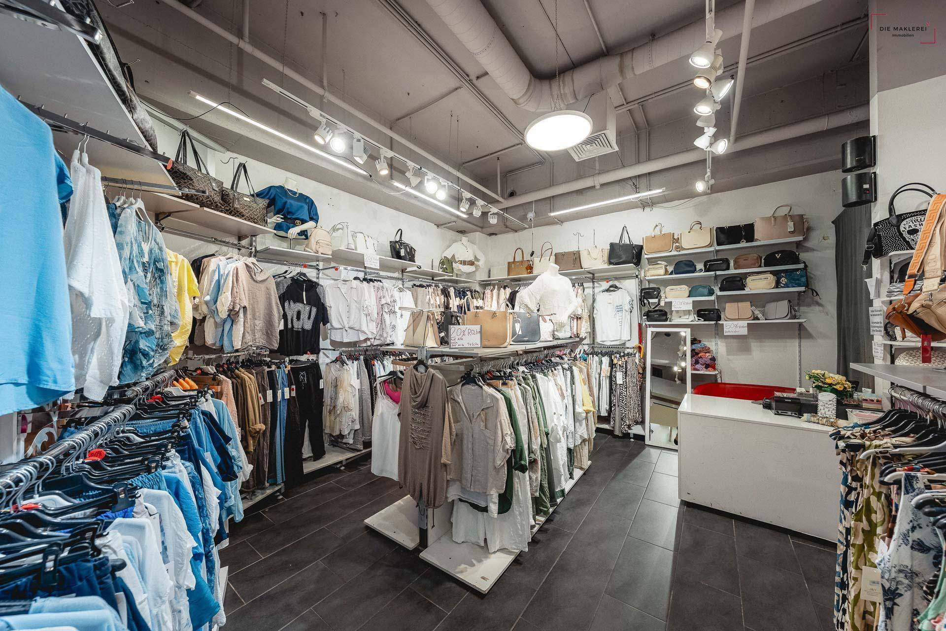 Längsansicht eines Bekleidungsgeschäfts mit Regalen voller Kleidung und Accessoires sowie Deckenbeleuchtung.