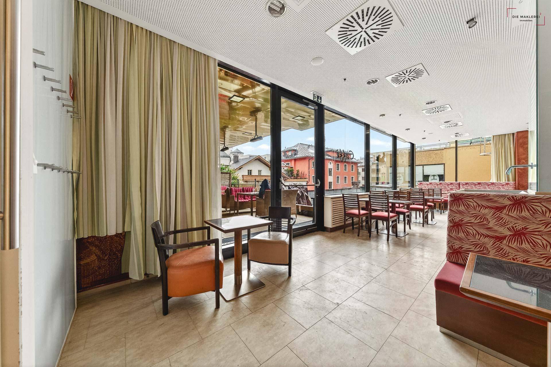 Gastronomiebereich mit Vorhängen und großen Fenstern, die einen Blick auf die Stadt ermöglichen.