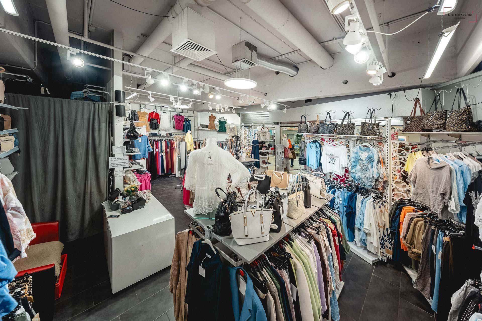 Blick in ein Bekleidungsgeschäft mit Schaufensterpuppen, Taschen und einer Umkleidekabine im Hintergrund.