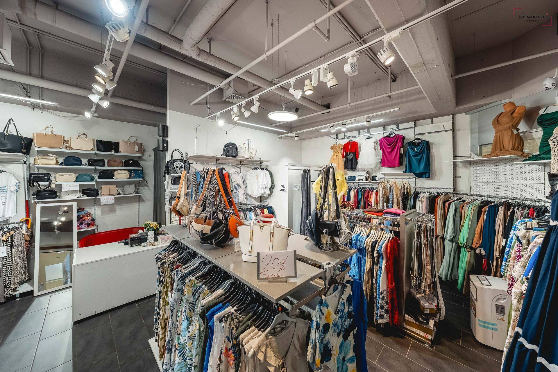 Innenansicht eines Bekleidungsgeschäfts mit Kleiderständern, Taschen und heller Deckenbeleuchtung.