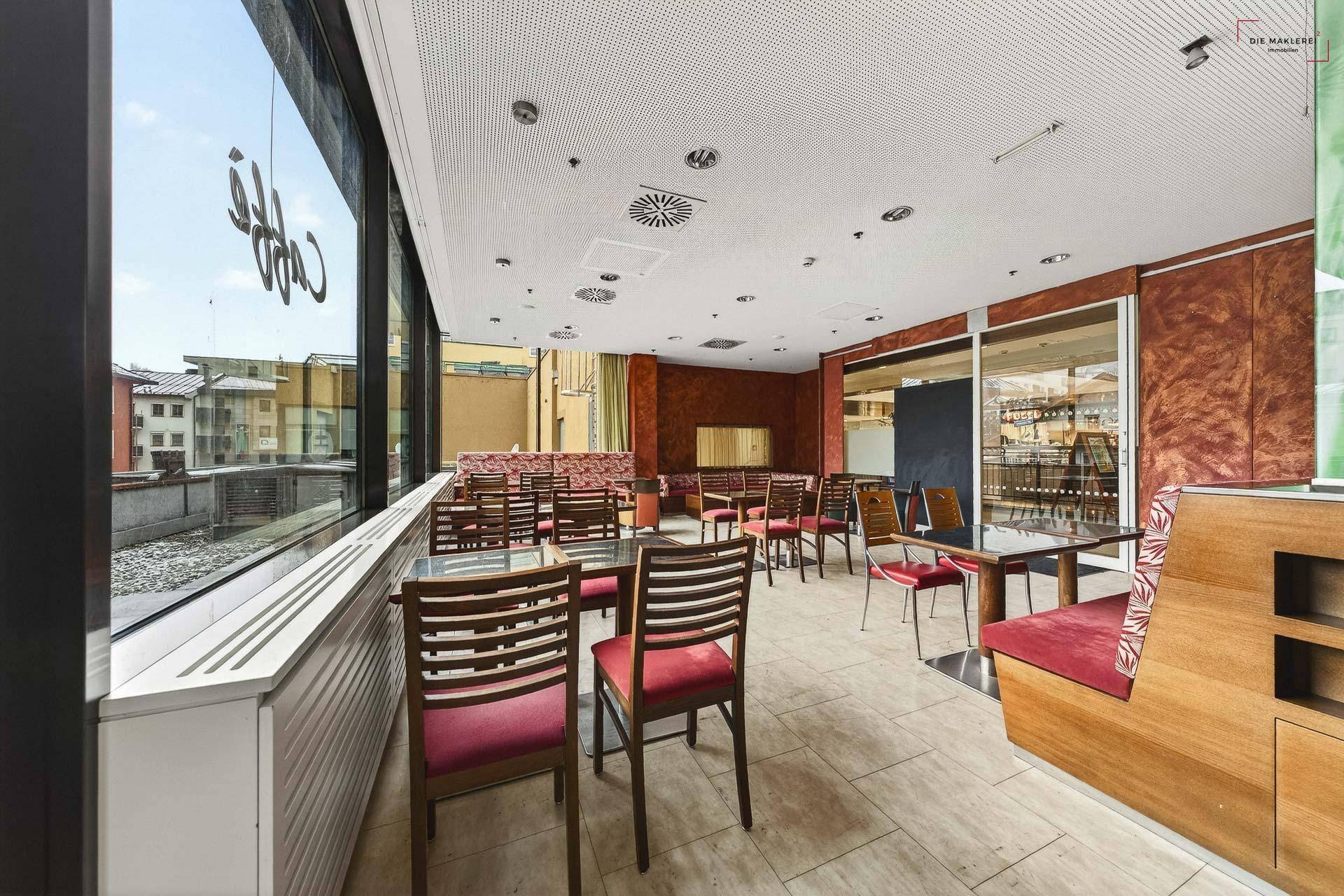 Gastronomiebereich mit "Café"-Schriftzug an der Fensterfront und Blick auf die umliegenden Gebäude.