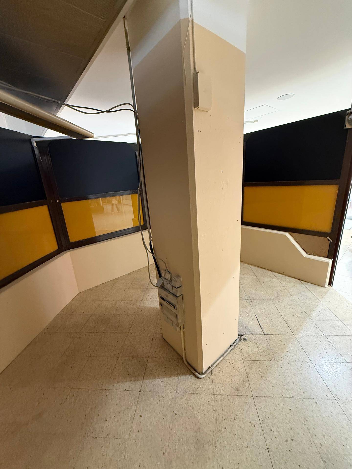 Seitenansicht des zentralen Pfeilers im Ladenlokal mit sichtbaren Kabeln und Installationsrohren.
