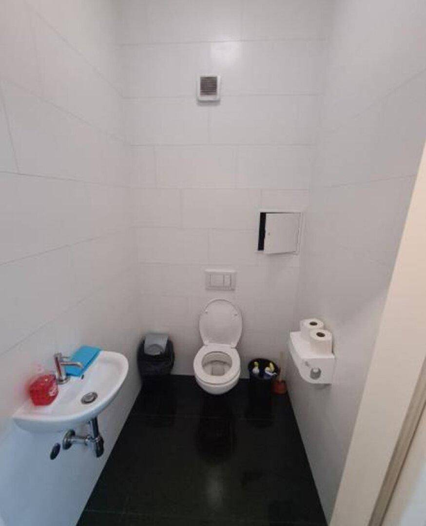 Kleiner Toilettenraum mit weißen Fliesenwänden, schwarzem Fliesenboden, WC und Waschbecken.