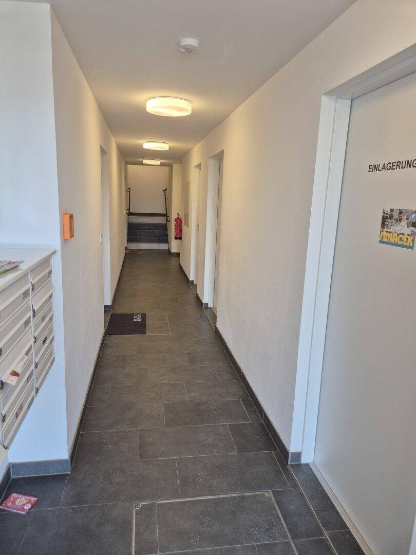 Langer, heller Flur mit dunklen Bodenfliesen, Briefkästen und Zugang zum Treppenhaus.