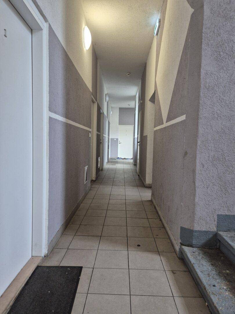 Langer, schmaler Flur mit Fliesenboden und mehreren Türen, der zu den Wohnungen führt.