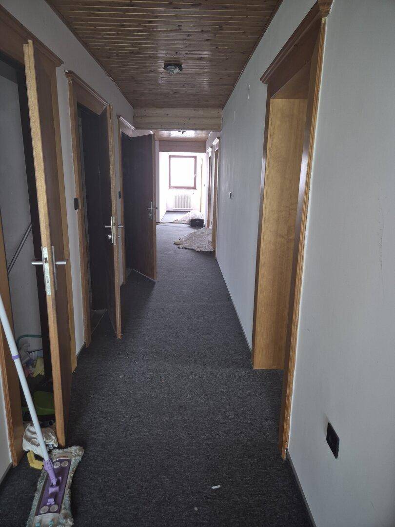 Langer Flur mit Teppichboden, Holztüren und Holzdecke, führt zu mehreren Zimmern.