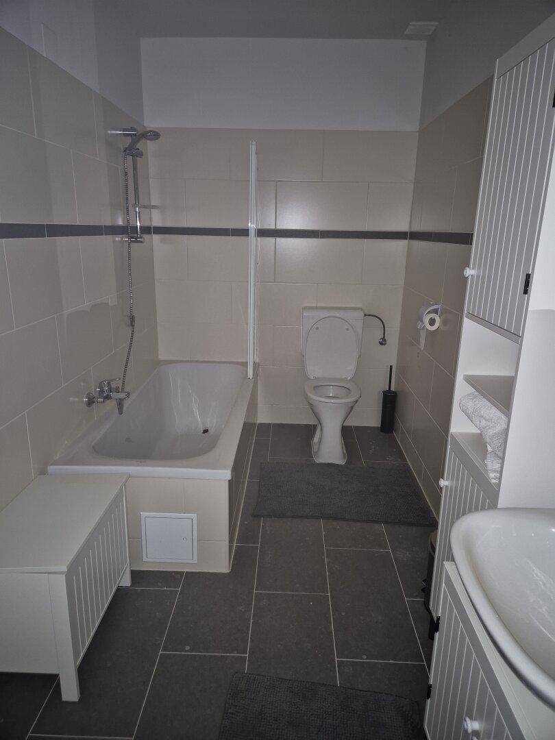 Badezimmer mit Badewanne, Toilette, Waschbecken und hellen Fliesen an Wänden und Boden.
