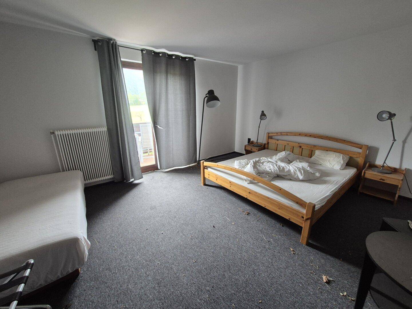 Schlafzimmer mit Doppelbett, Teppichboden und Zugang zu einem Balkon.