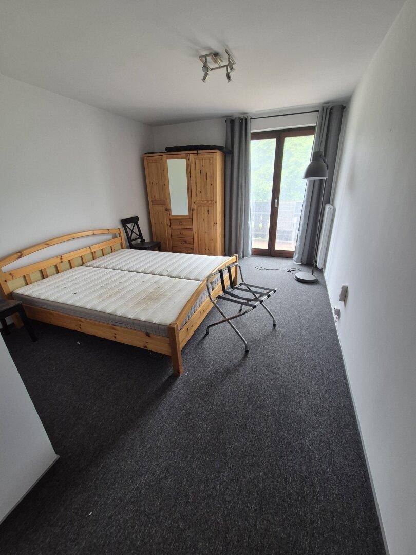 Schlafzimmer mit zwei Einzelbetten, Holzschrank und Zugang zu einem Balkon.