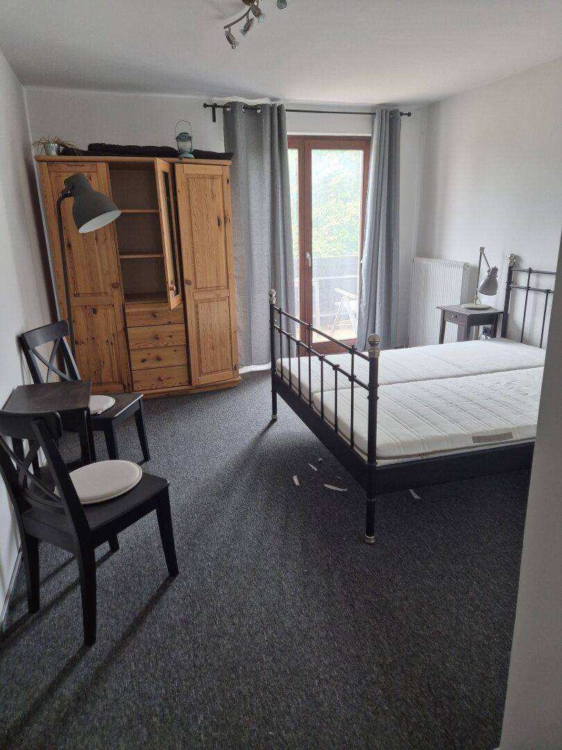 Schlafzimmer mit Metallbett, Holzschrank und Balkontür, hell und einfach eingerichtet.