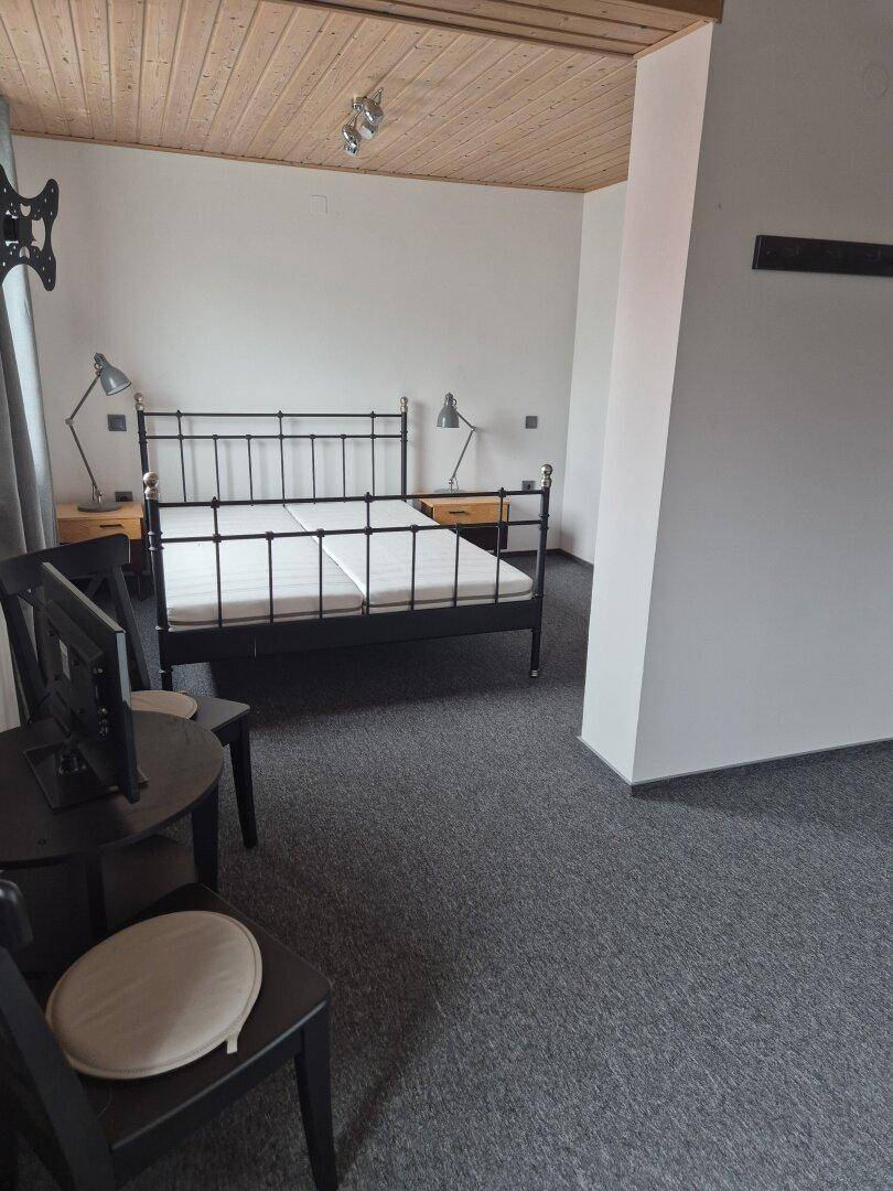 Schlafzimmer mit Metallbett, Holztäfelung an der Decke und Teppichboden.