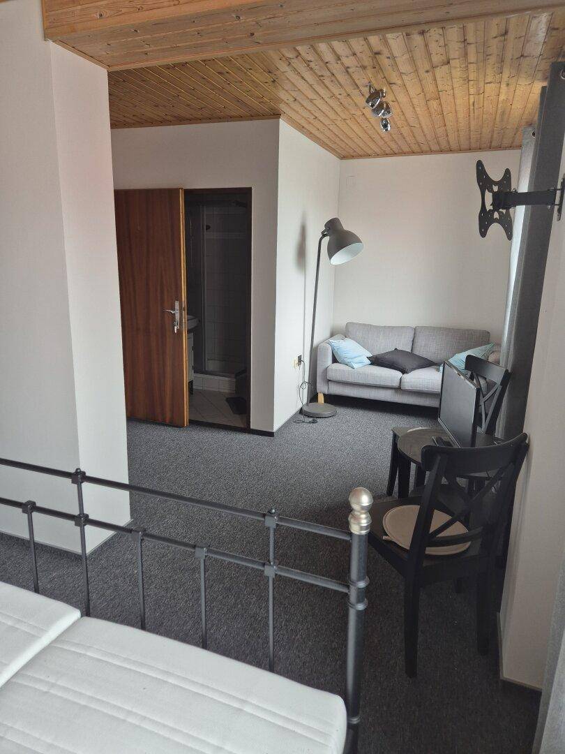 Gemütliches Schlafzimmer mit Holzbalkendecke, grauem Teppichboden und Zugang zu einem Badezimmer.
