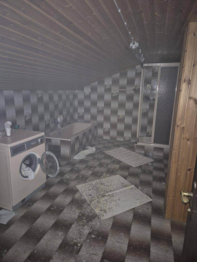 Badezimmer mit Badewanne, Dusche, Waschmaschine und gemusterten Fliesen unter einer Holzdecke.