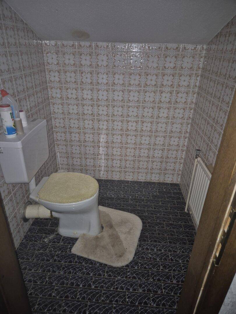 Kleines WC mit Toilette und gemusterten Fliesen an den Wänden und auf dem Boden.