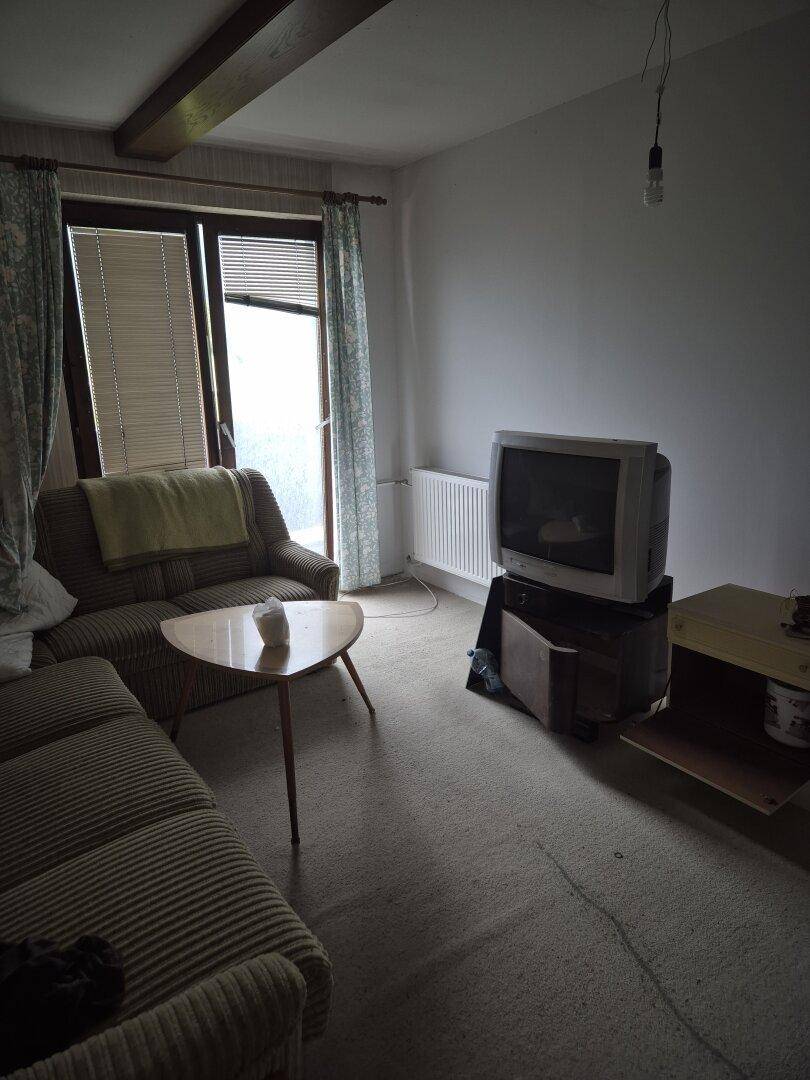 Wohnzimmer mit zwei Sofas, Couchtisch und einem alten Fernseher, mit Zugang zum Balkon.